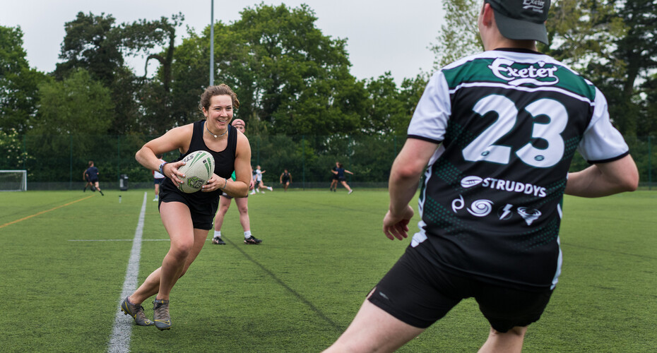 A rugby player holding the ball, attempts to dodge around an opponent player